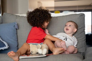Two siblings laugh while tickling each other playfully on a cozy sofa
