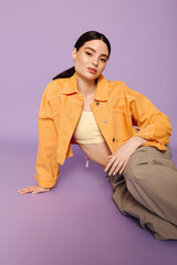 Young woman in stylish outfit poses elegantly against a vibrant purple backdrop