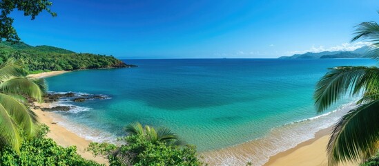A breathtaking panoramic view of a tranquil blue sea with sandy beach and lush green vegetation under clear skies ideal for vacation imagery