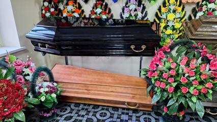 Elegant black and wooden coffins with colorful floral arrangements in funeral home display.