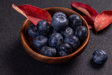 Fresh ripe blueberries with autumn leaves in wooden bowl on dark background