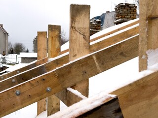 Workers are building a wooden framework amid snow-covered ground near houses during the winter season