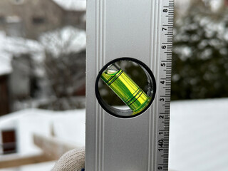 A leveling tool with a bright green bubble indicates perfect alignment on a snowy construction site in winter