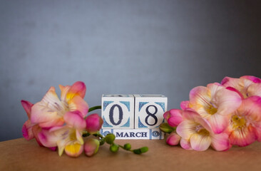 Concept of greeting card on March 8 International Women's day with wooden calendar decorated with freesia flower and copy space.