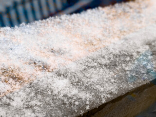 Fresh snow accumulates on a wooden surface, creating a serene winter scene in a quiet rural setting at dawn