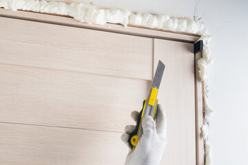 installation of interior door frame, close-up, knife in worker's hands, mounting foam