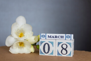Concept of greeting card on March 8 International Women's day with wooden calendar decorated with freesia flower and copy space.