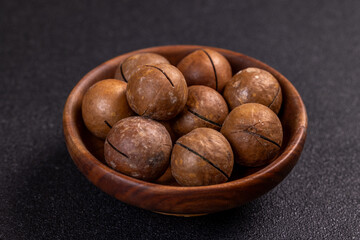 Macadamia nuts piled in wooden bowl on dark background