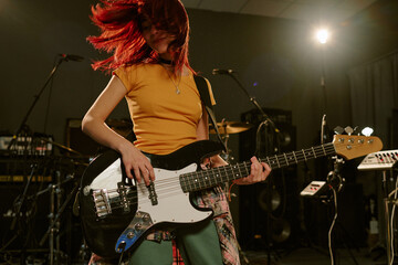 Low angle shot of unrecognizable teen girl shaking head while playing guitar solo at studio