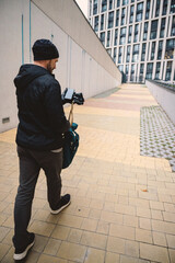A man walks against the backdrop of modern urban architecture. He is dressed for autumn and has a...
