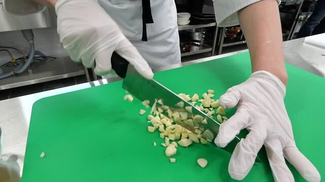 Chef chopping garlic on a green cutting board