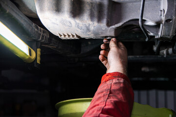 Mechanic Removing Oil Drain Plug to Drain Engine Oil During Car Maintenance in Auto Repair Shop