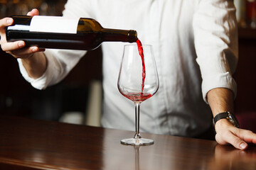 Male sommelier pouring red wine into long-stemmed wineglasses.