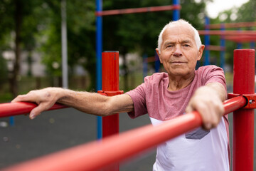 Obraz premium Senior sporty man performs various exercises on uneven bars in park