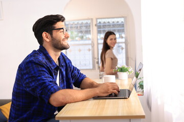 Business couple working, communicating while sitting at the office desk together. Cheerful couple, calm asian woman and caucasian man working at home with laptop together.