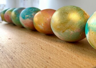 A series of vibrant decorative spheres in shades of blue, gold, and peach are neatly lined up on a wooden table surface, illuminated by natural light