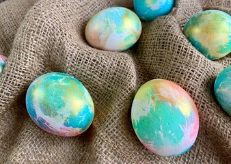 Brightly colored decorative eggs in shades of blue, pink, and yellow are arranged on a rustic burlap surface, adding a festive touch for spring celebrations and Easter gatherings