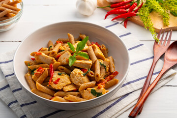 Stir fried whole wheat Penne rigate pasta with chicken breast in white plate.Pad Kra Pao,Thai fusion food.