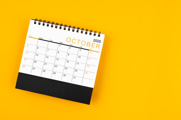 October 2025 desk calendar on yellow background, position with copy space.