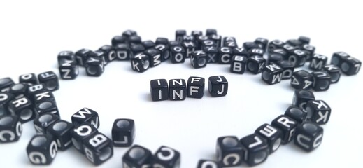 Scattered black plastic cubes, focus on the letters INFJ in the center. The foreground and background are blurred. INFJ is one of the 16 personality types identified by the MBTI test.