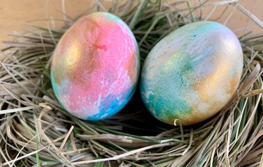 Two beautifully painted Easter eggs with vibrant colors rest in a straw nest, showcasing creative artistry and the joyful spirit of springtime festivities