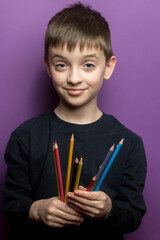 A young student’s hands holding multiple colored pencils, symbolizing creativity, learning, and artistic expression. Close-up shot with a bright purple background. 