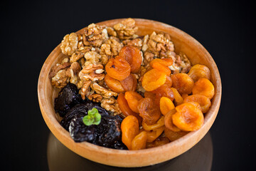Prunes, dried apricots and nuts in a wooden bowl on a dark background