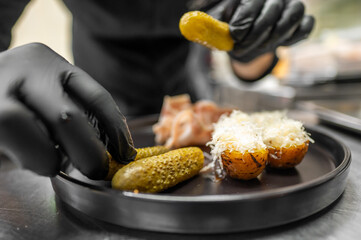 A chef in black gloves arranging pickles on a dark plate. Delicious stuffed potatoes topped with...