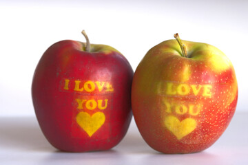 Two apples with ‘I Love You’ written on them, placed on a white background.