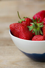 A close-up shot features a bowl overflowing with ripe red strawberries against a blurred, wooden...