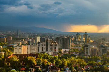Top view of the Kazakh city of Almaty against the backdrop of a rain cloud at sunset