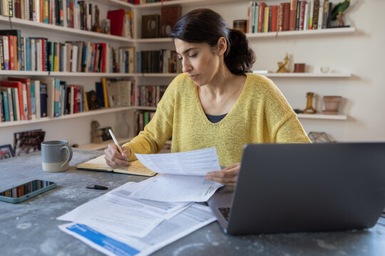 Woman diligently taking notes and studying bills and personal finance