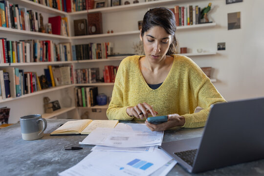 Woman using calculator while managing bills and personal finance