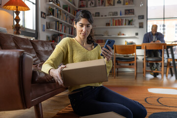 Woman using a smartphone whilst holding a delivery box
