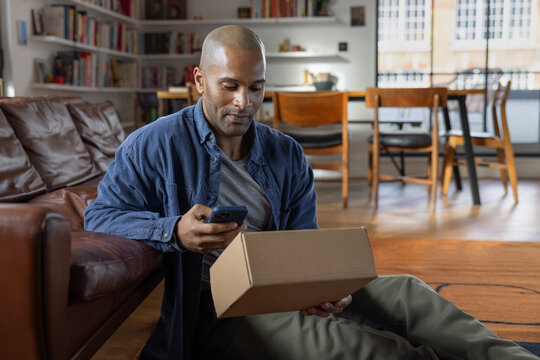 Man using a smartphone whilst holding a delivery box
