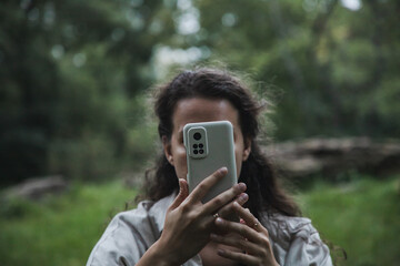 A girl is glued to her phone in nature. A girl can't relax without her phone. A girl reads the news, sits on social networks.