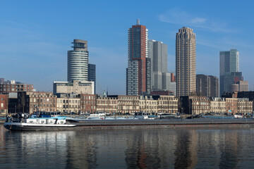 Skyline with skyscrapers of Rotterdam with in the foreground typical dutch architecture with brick facades of a few stories high. cargo ships in the maashaven.