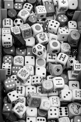 A black and white photograph captures a dense collection of dice, varying in size and style, piled...