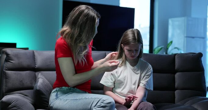 Worries woman checks little daughter body temperature with sitting on sofa. Mother reveals fever disease symptoms examining girl at home slow motion