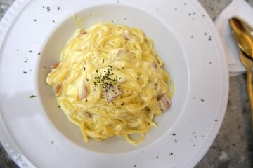 Creamy spaghetti carbonara served on a white plate, garnished with herbs and featuring a rich cheese sauce with bacon, close up and high angle view