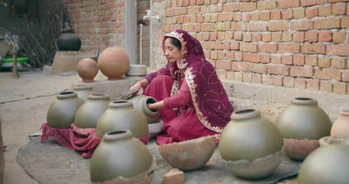 Indian village woman wear traditional saree sitting outdoor make hand made potters finishing touches clay pots Asian young gen x female lady learn handcraft create sculptor pottery mud product outside