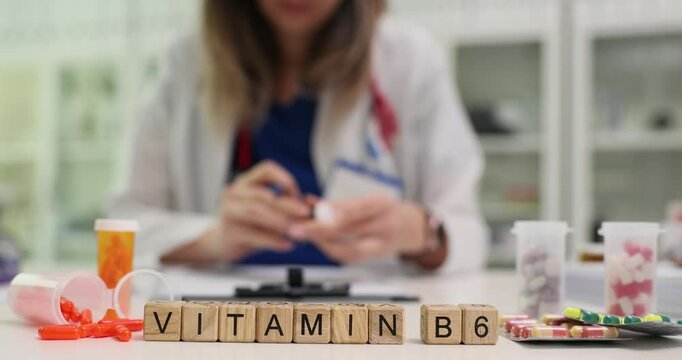 Professional woman doctor recommends vitamin B6 to patient. Miniature wooden cubes form phrase VITAMIN B6 on table in clinic office. Slow motion