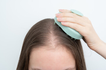 Woman using a scalp massager to stimulate hair growth and care for scalp with copy space. Concept of beauty treatment, wellness, and addressing alopecia and thinning hair through daily routines.