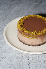 Dubai chocolate cheesecake with pistachio paste and kataifi filling covered in chocolate ganache on white plate. Grey background with copy space. Vertical photo. Indulgence, gourmet desserts.
