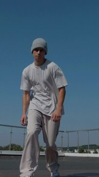Vertical. The guy coolly dances breakdance on the roof of the house. A man dances an energetic athletic dance. Man effortlessly break dancing on a rooftop. Urban dancer showing off skills on rooftop. 