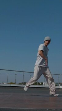 Vertical. The guy coolly dances breakdance on the roof of the house. A man dances an energetic athletic dance. Man effortlessly break dancing on a rooftop. Urban dancer showing off skills on rooftop. 