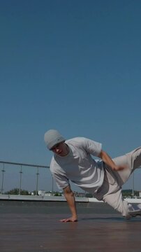 Vertical. The guy coolly dances breakdance on the roof of the house. A man dances an energetic athletic dance. Man effortlessly break dancing on a rooftop. Urban dancer showing off skills on rooftop. 