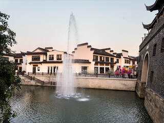 Tranquil Waterfront View with Fountain and Traditional Architecture at Dusk