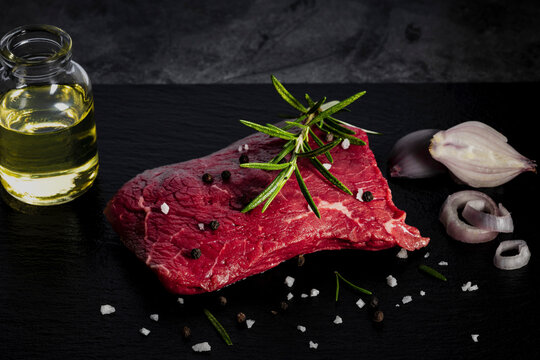 Raw, lightly marbled beef steak with pepper, salt and rosemary
