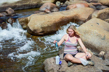 Happy young hiker girl purifying water at Merced River edge in Yosemite National Park.